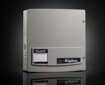 Gray metal fire alarm control cabinet with labeled panels on the lower front, including 'FIRE ALARM INTERFACE' and 'Vigilon' branding, set against a dark background.